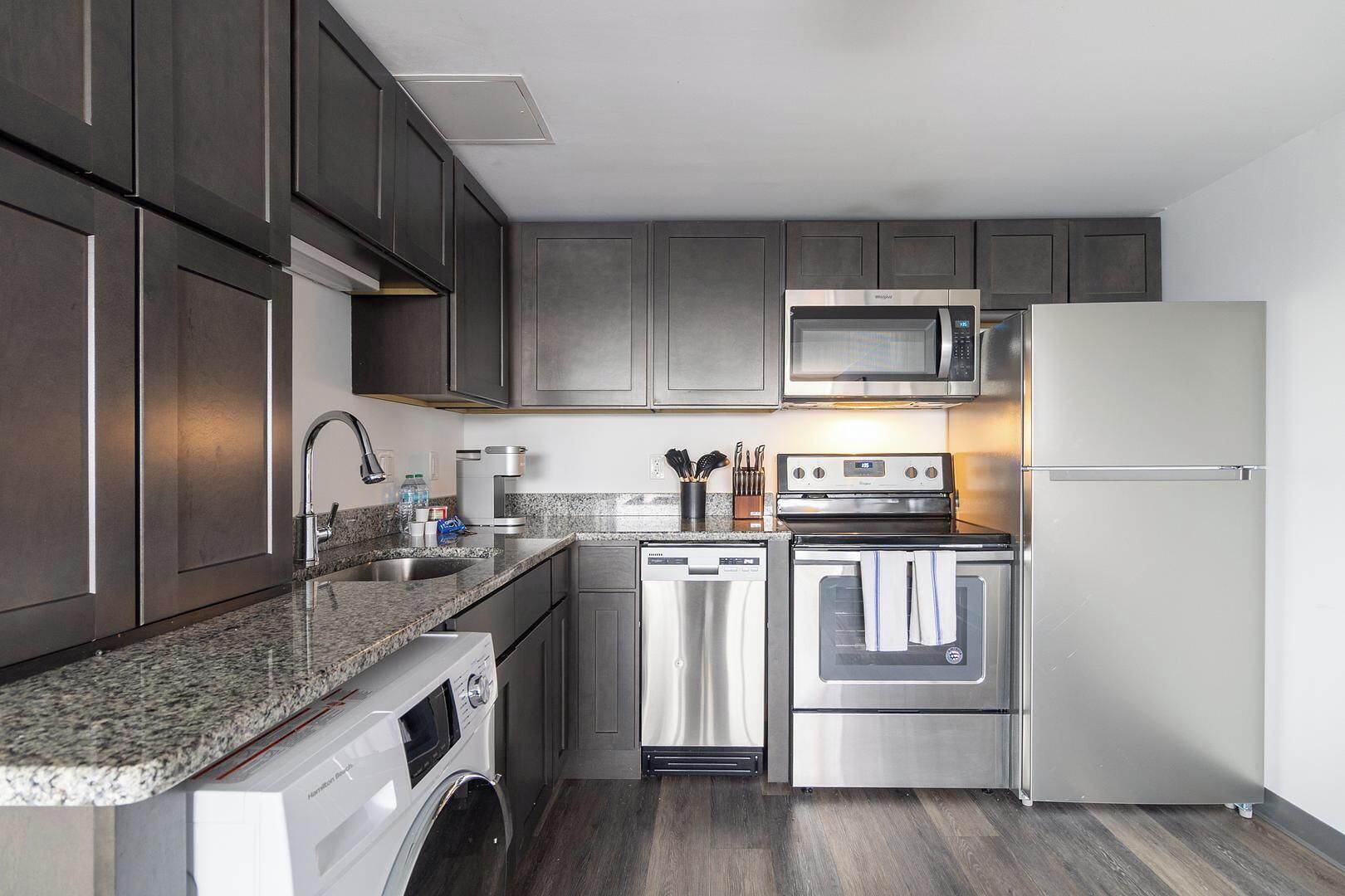 Una cocina moderna con electrodomésticos de acero inoxidable, horno integrado, microondas y lavavajillas, además de un refrigerador grande.