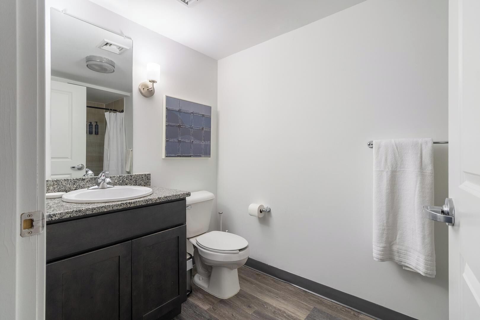 A modern bathroom with a granite countertop sink, a white toilet, and a towel hanging on the door.
