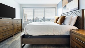 Een moderne slaapkamer met een bed, een houten dressoir en een groot raam met jaloezieën.