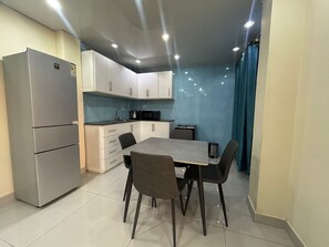 A compact kitchen with a refrigerator, microwave, and sink. There is a dining table with chairs. - Moima Plaza Guesthouse (Monrovia)