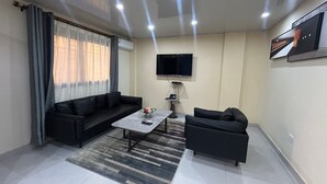Un salon moderne avec un canapé noir, une table basse, un téléviseur et un tapis à motifs.