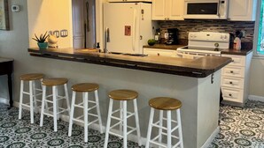 Una cocina con armarios blancos, una isla central con taburetes, un refrigerador, un microondas y una estufa.
