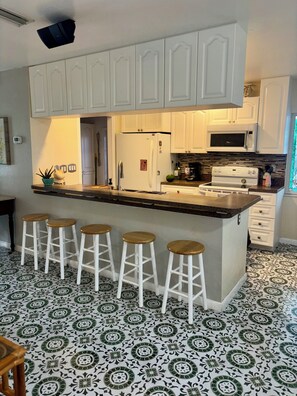 A kitchen with white cabinets, a central island with stools, a refrigerator, a microwave, and a stove. - Cozy Port Charlotte Getaway- Near Hospitals, Beaches (Port Charlotte)