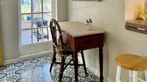 Un comedor con una mesa de madera, una silla, un taburete, un termostato en la pared y un ventanal con vistas al exterior.