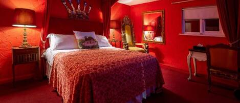 A room with a large bed, a nightstand, a mirror, and a window with curtains.