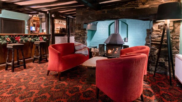 A cozy room with a stone fireplace, red upholstered chairs, and a patterned carpet. - The lion hotel  (Berriew)