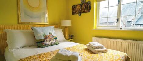 A hotel room with a bed, a window, a painting, and a radiator.