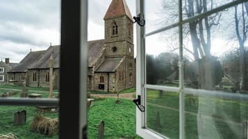 A view through a window of a church with a prominent tower, a grassy cemetery, and stone buildings.