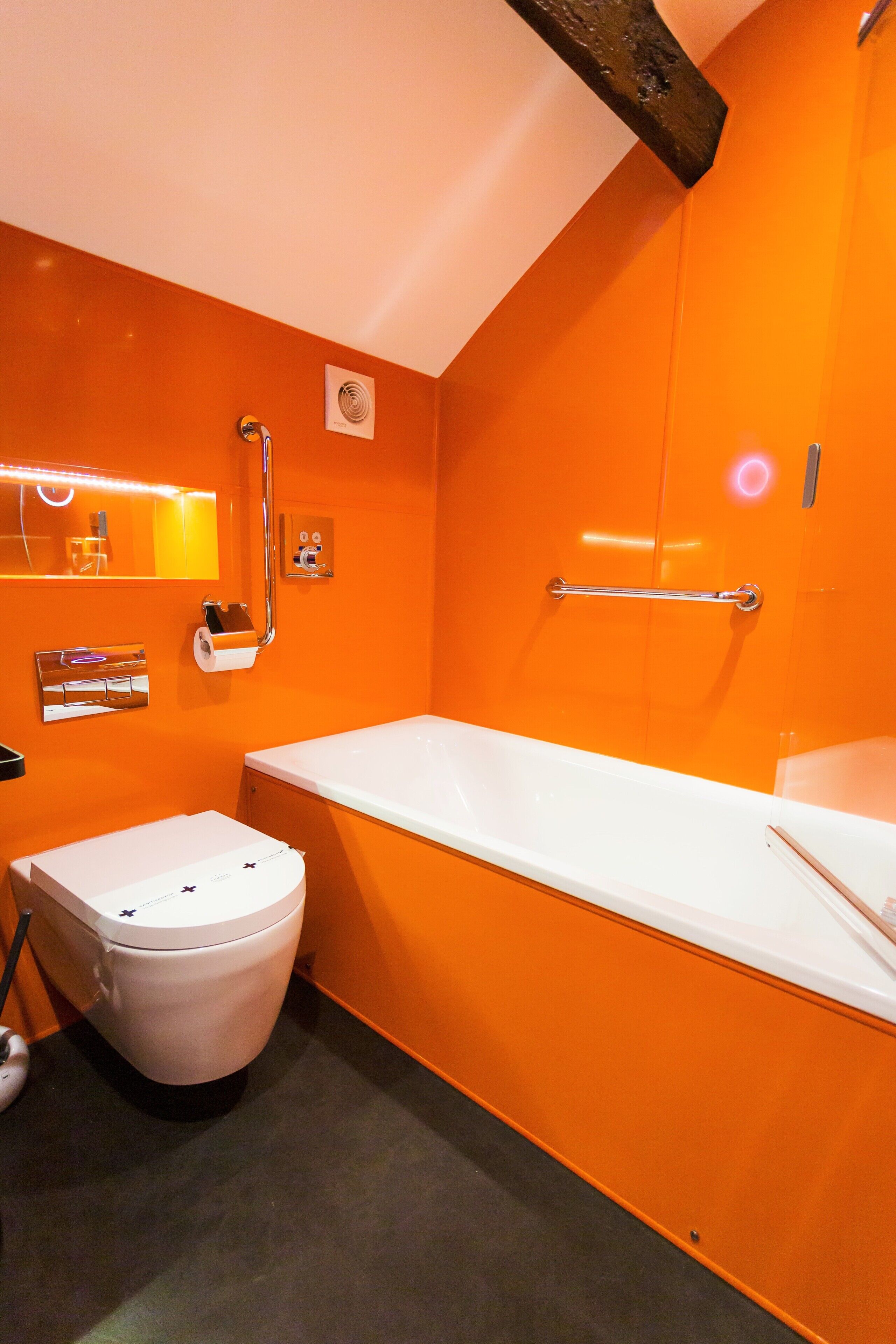 A bathroom with a white bathtub, a white toilet, and an orange wall.