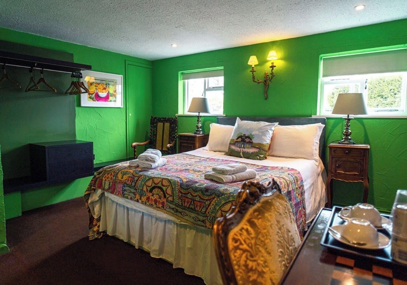 A green-themed bedroom with a bed, two bedside tables, a chair, and a wall-mounted TV.