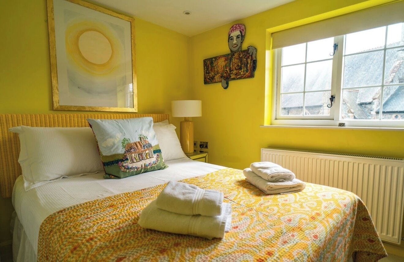 Une chambre d’hôtel avec un lit, une fenêtre, un radiateur et des œuvres d’art accrochées aux murs.