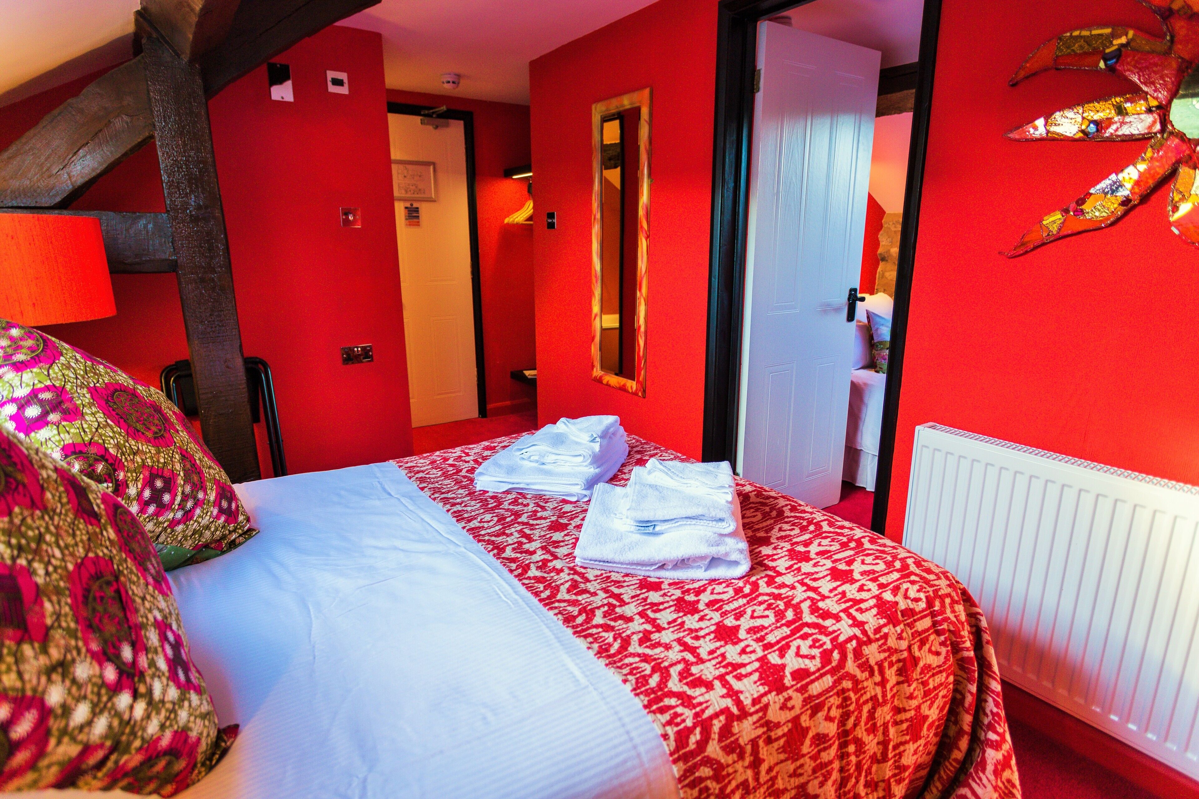 Une chambre d’hôtel avec un mur rouge, un lit avec une literie blanche et rouge, un miroir et un radiateur.