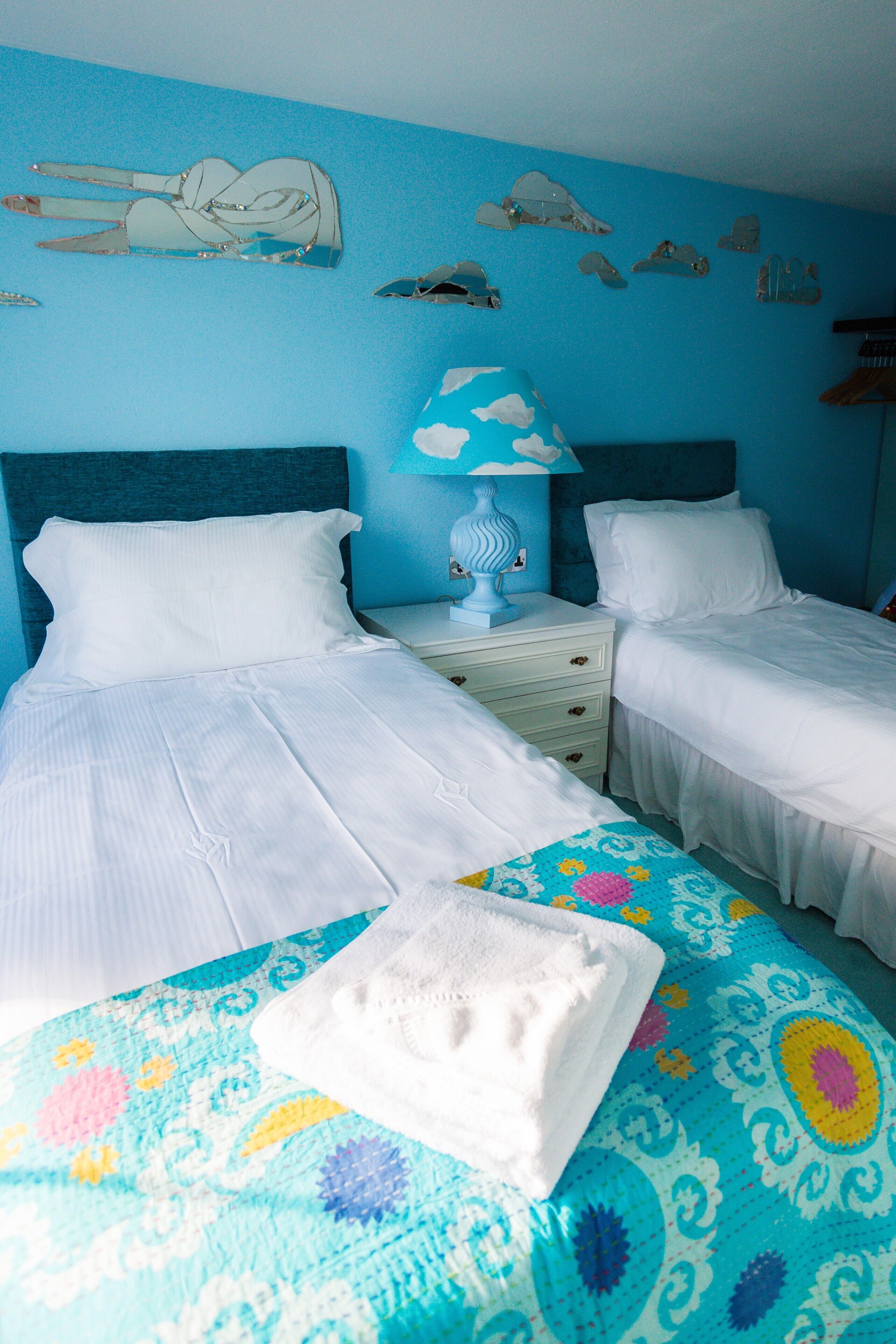 A room with two beds, a nightstand, a lamp, and wall decorations.
