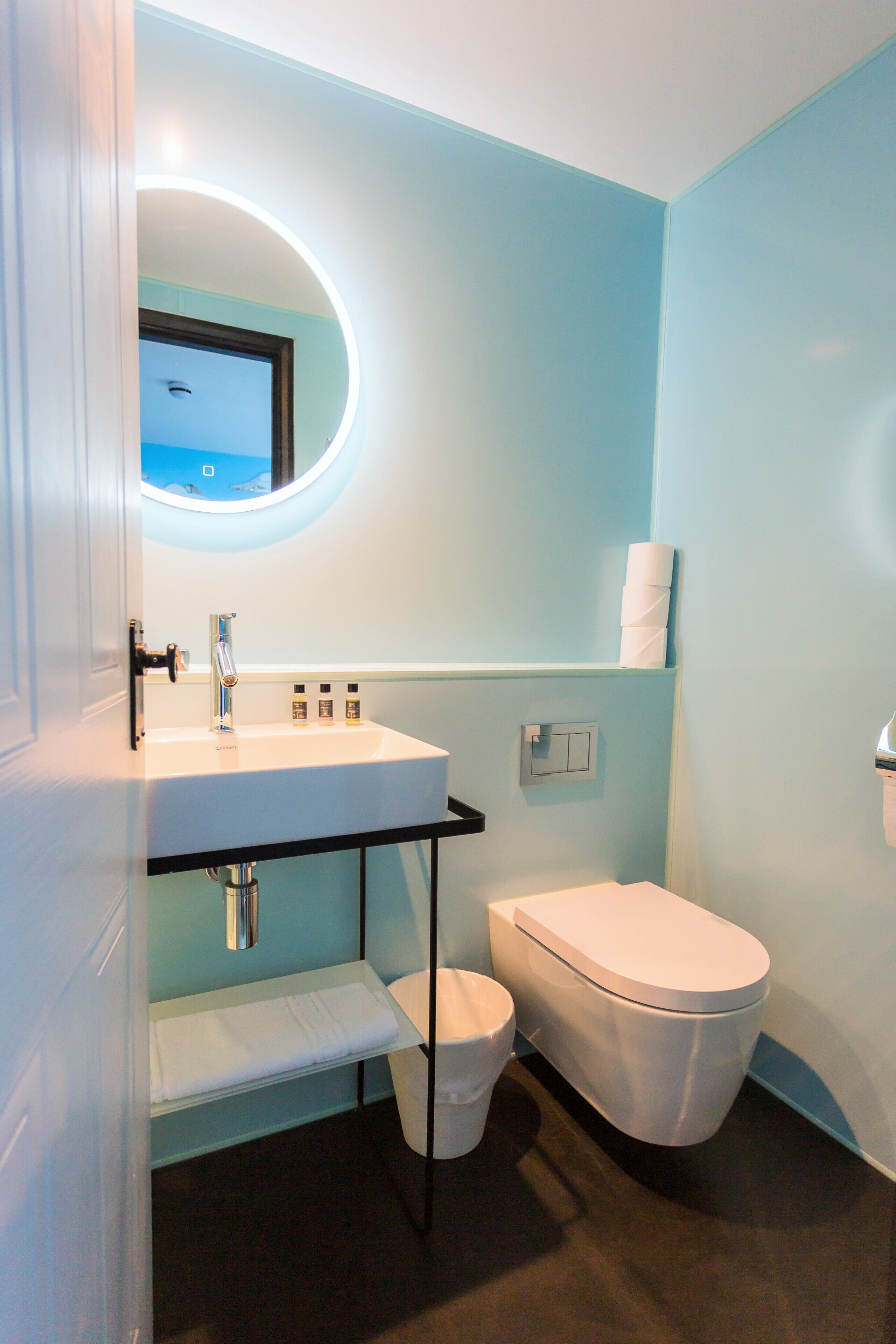 Un baño con un lavamanos blanco, un inodoro y un espejo con luz circular.