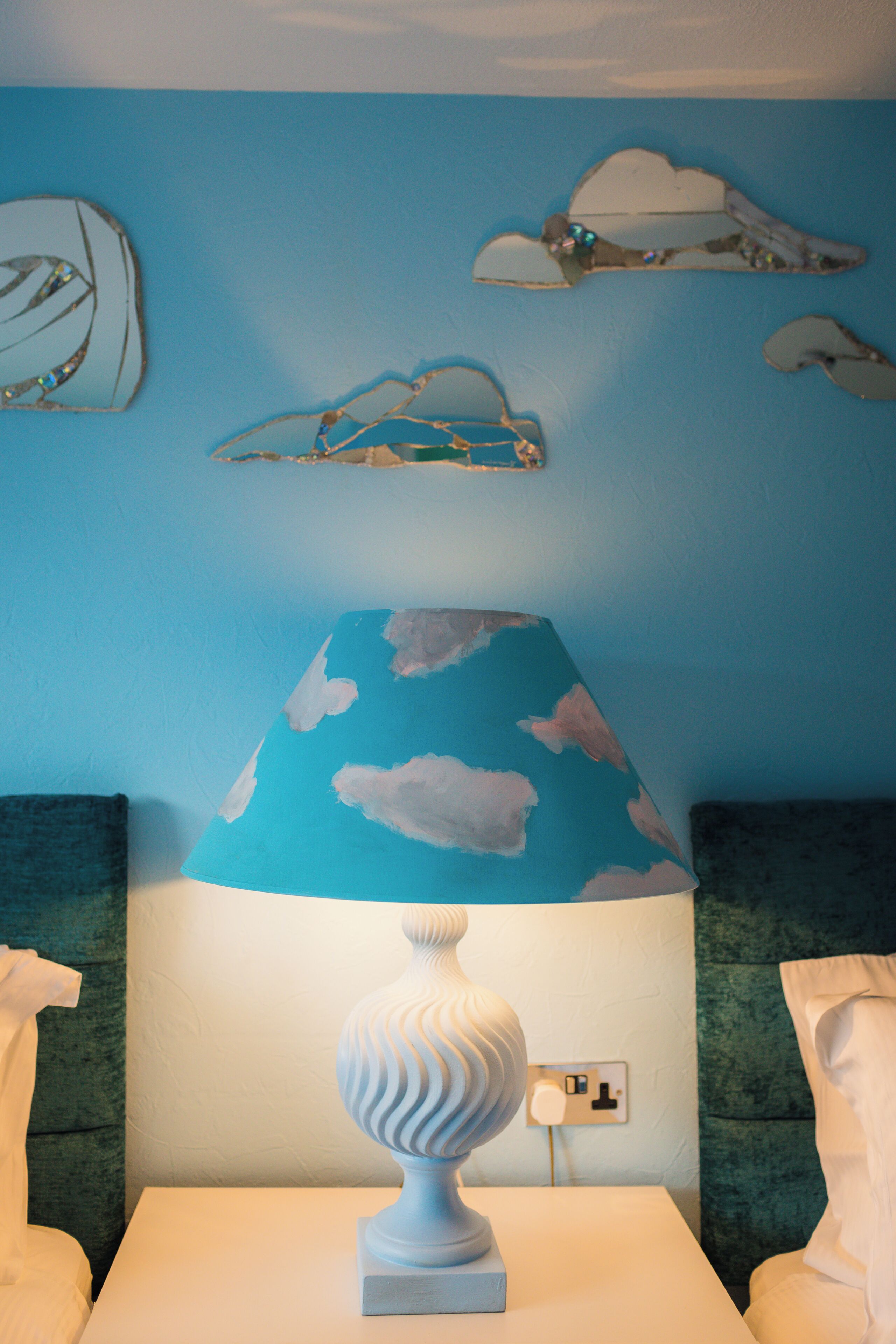 A room with a white table, a blue lamp with cloud patterns, and a wall with cloud-shaped decorations.
