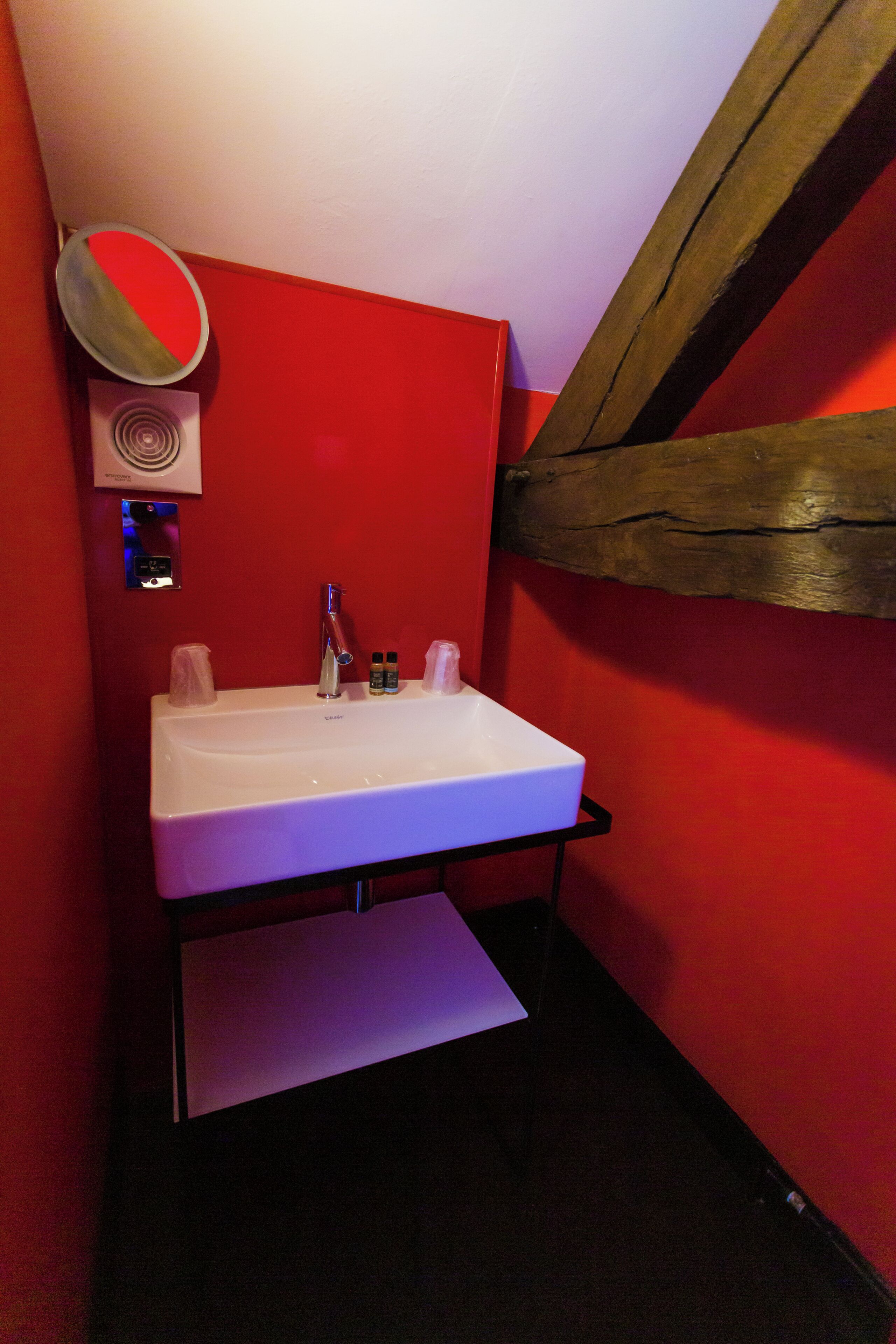 Een badkamer met een wit wastafelmeubel, rode wanden en een houten balk.