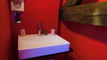 Een badkamer met een wit wastafelmeubel, rode wanden en een houten balk.
