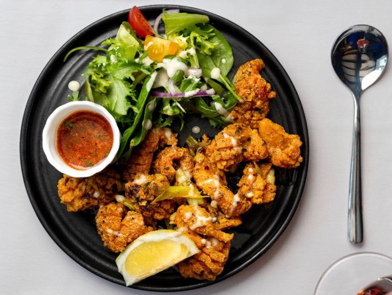 A plate of fried chicken with a side salad and a small bowl of sauce.