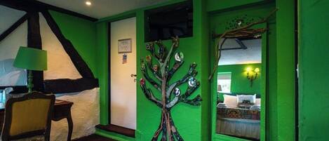 Ein Zimmer mit grüner Wand, einer Baum-Wandmalerei, einem Bett und einem Sessel.