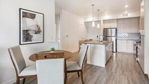 A modern kitchen with a central island, stainless steel appliances, and a dining area with a round table and chairs. - Landing | Incredible 2BD, Gym, Clubhouse (Mesa)