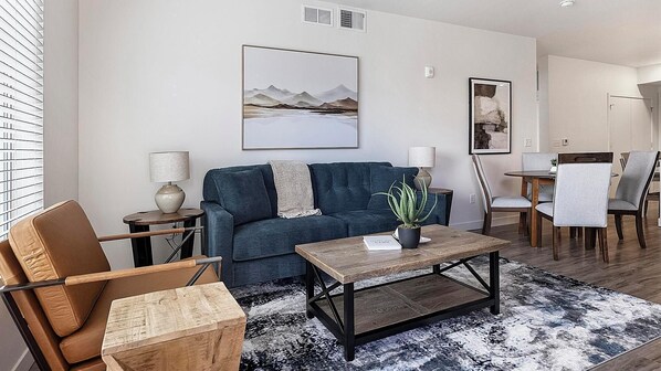 A modern living room with a sofa, coffee table, and chairs, a dining area with a table and chairs, and artwork on the walls. - Landing | Incredible 2BD, Gym, Clubhouse (Mesa)