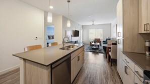 A modern kitchen with a central island, built-in appliances, and a dining area with a coffee machine. - Landing | Amazing 1BD, Clubhouse, Pool (Mesa)