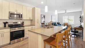 A modern kitchen with stainless steel appliances, wooden cabinets, and a central island with bar stools. - Landing | Chic 1BD, Pool, Gym (Mesa)