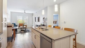 A modern kitchen with a central island, a dining area with chairs, a built-in dishwasher, and a ceiling fan. - Landing | Chic 1BD, Pool, Gym (Mesa)