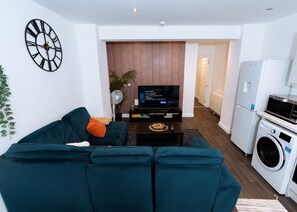 Ein modernes Wohnzimmer mit einer Couch, einem Fernseher, einem Ventilator und einer Küchenzeile mit einer Waschmaschine.