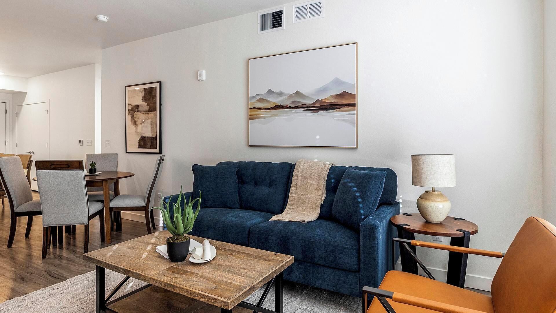 A living room with a blue sofa, a wooden coffee table, a lamp, and a painting on the wall.