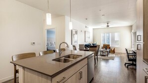 Een moderne keuken met een centraal eiland, een eethoek met een tafel en stoelen, en een zithoek met een bank en televisie.
