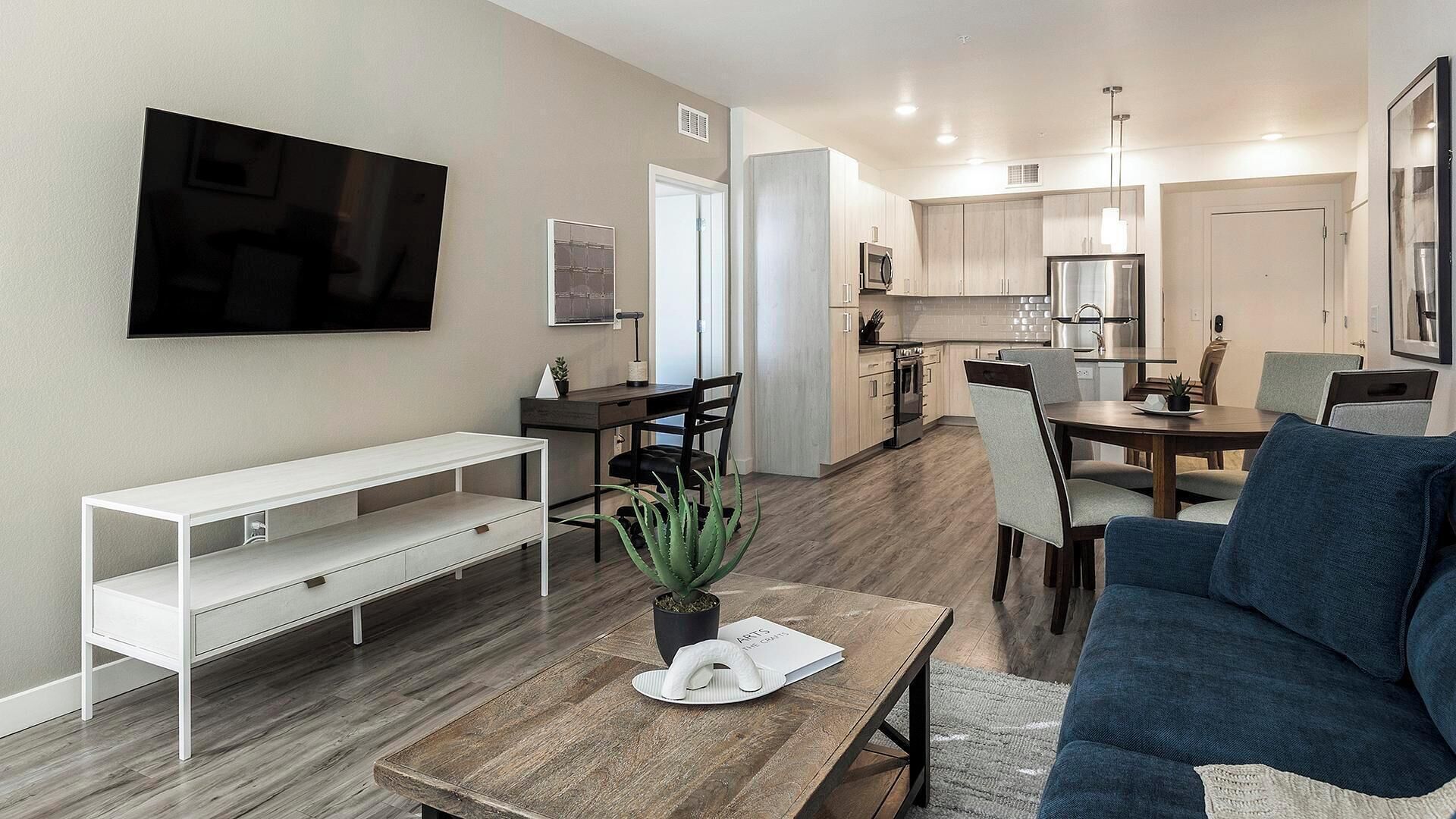 A modern living room with a flat-screen TV, a white console table, a blue sofa, and a wooden coffee table with a plant.
