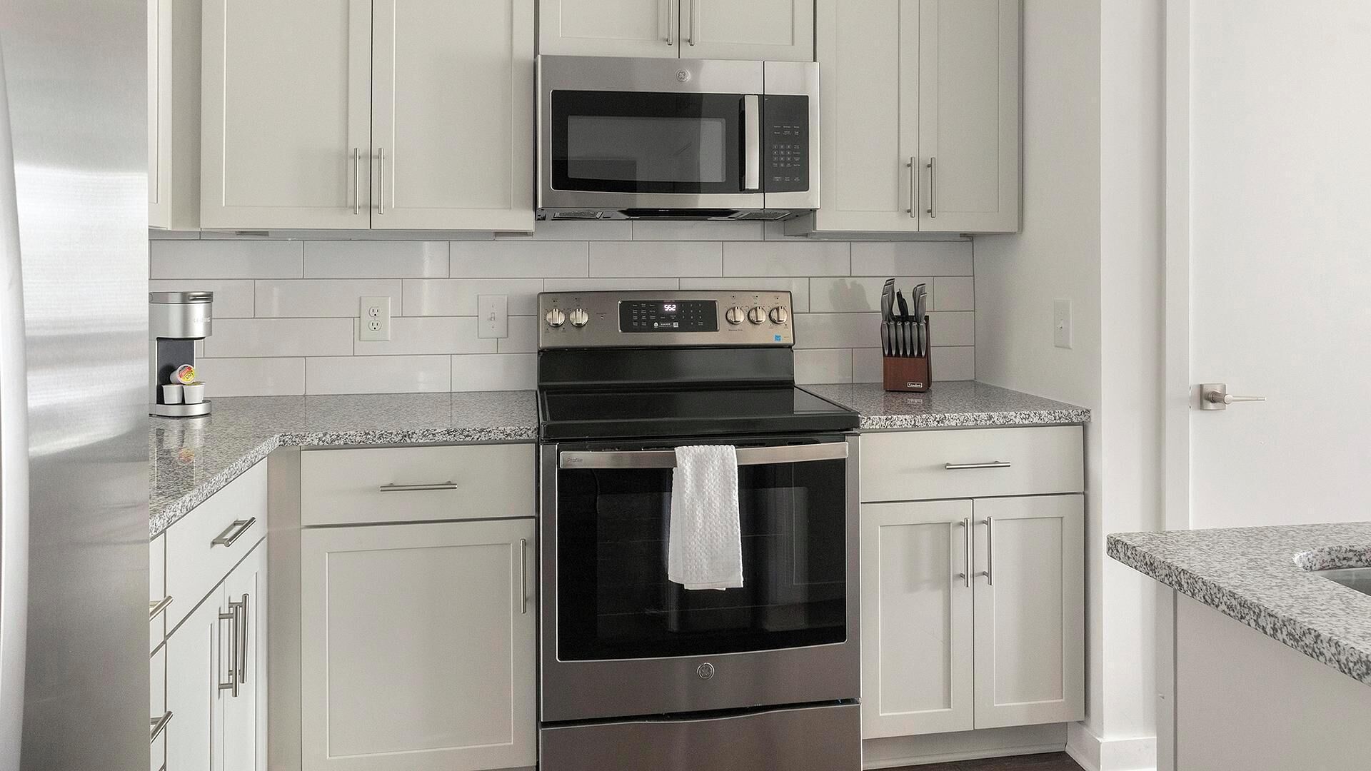 A kitchen with white cabinets, a stainless steel oven, a microwave, and a coffee maker.