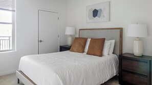 A bedroom with a bed, two bedside tables, a door, and a window. - Landing | Spectacular 2BD, Clubhouse, Gym (Raleigh)