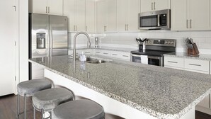 A modern kitchen with white cabinets, stainless steel appliances, a granite countertop, and bar stools. - Landing | Beautiful 2BD, Clubhouse, Yoga Studio (Raleigh)