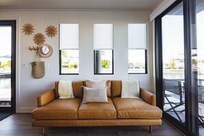 A modern living room with a leather sofa, decorative wall art, and large windows offering a view of the outdoors. - Waterfront & Heated Pool - Break Awai Floating Villa (Stock Island)