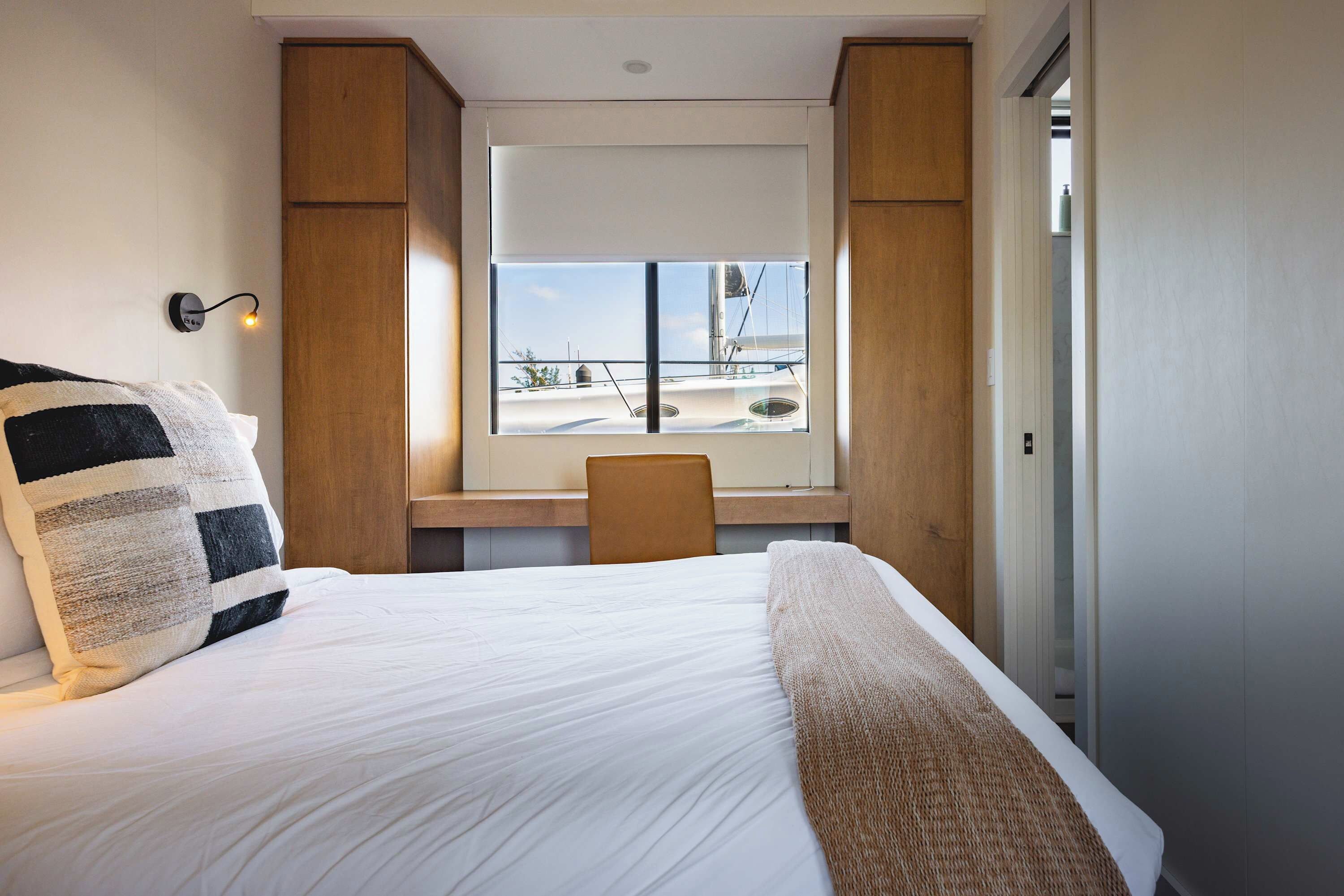 A hotel room with a bed, a desk, and a window with a view of a sailboat.