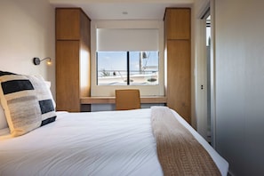 Habitació d'hotel amb llit, escriptori i finestra amb vista a un veler.
