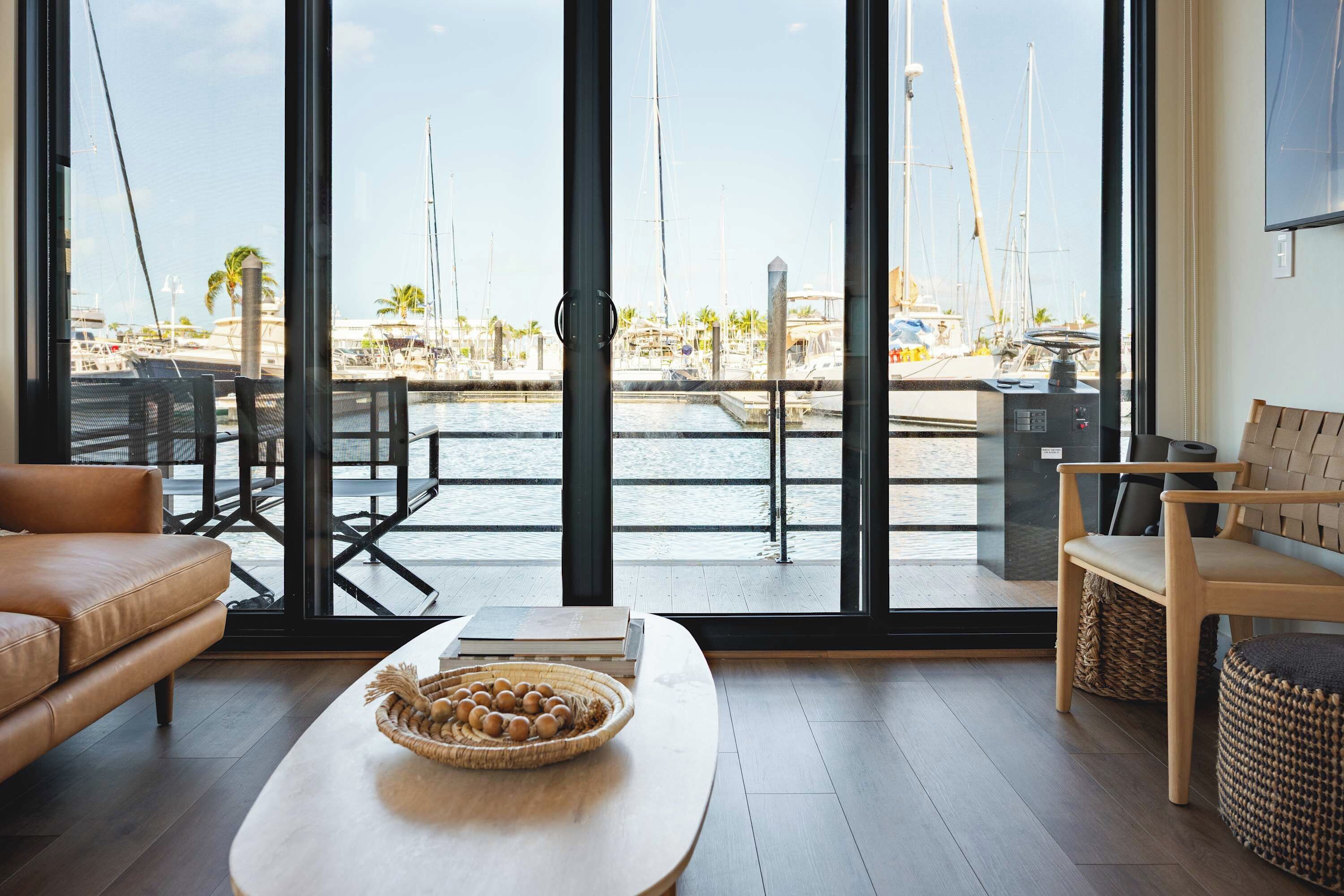 Una sala de estar moderna con un amplio ventanal con vistas a un puerto deportivo y barcos.
