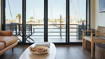Una sala de estar moderna con un amplio ventanal con vistas a un puerto deportivo y barcos.