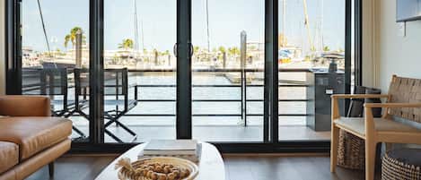 Una sala de estar moderna con un amplio ventanal con vistas a un puerto deportivo y barcos.
