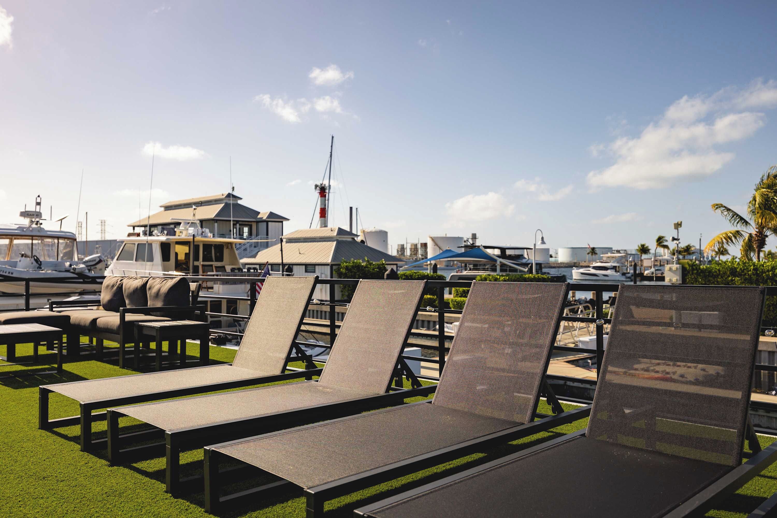 Outdoor lounge chairs on artificial grass with a marina and boats in the background.