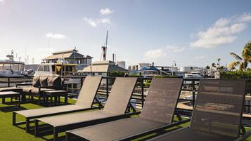 Outdoor lounge chairs on artificial grass with a marina and boats in the background.