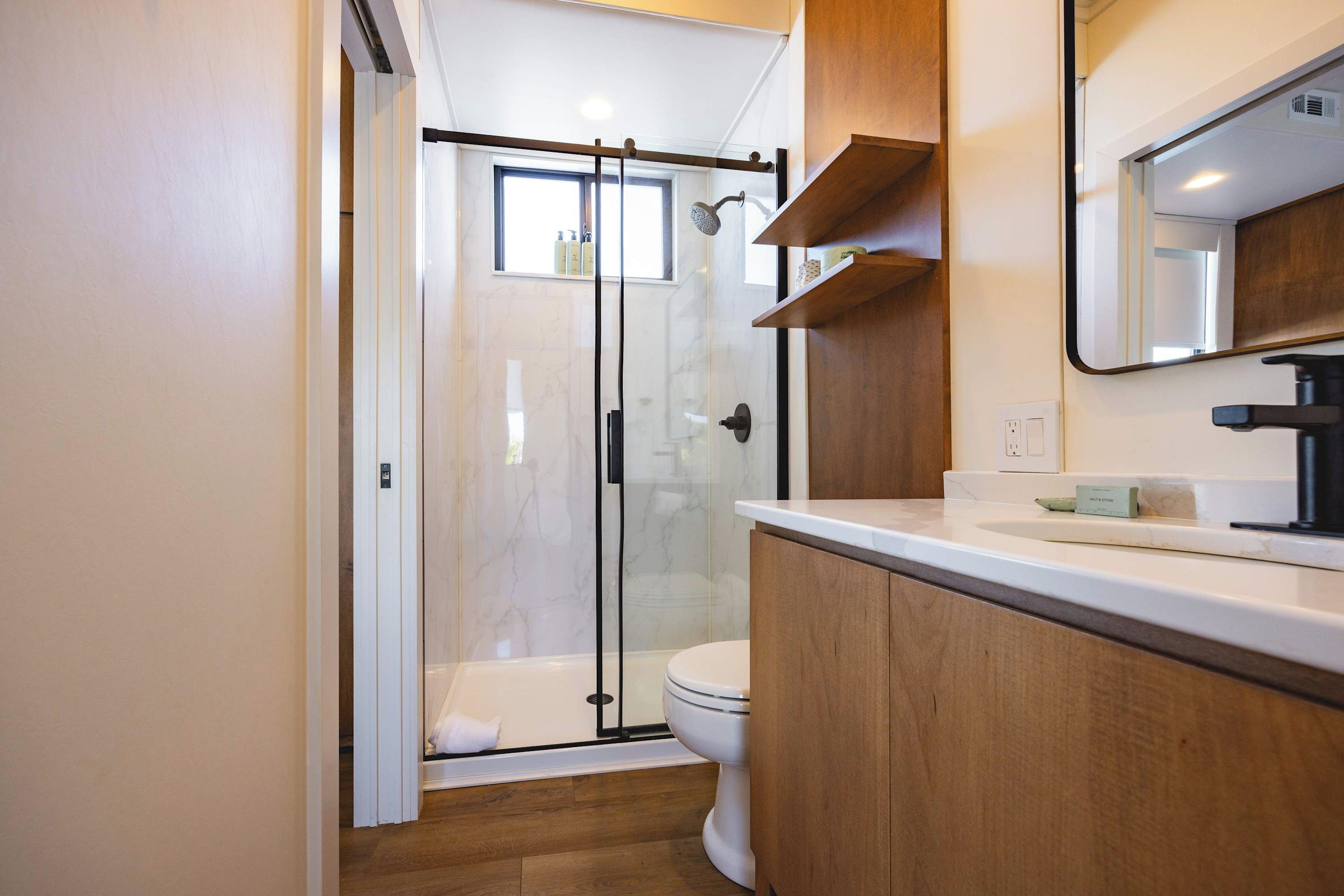 Une salle de bain moderne dotée d’une douche à parois de verre, de toilettes et d’un meuble-lavabo avec un miroir.
