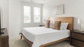 Een slaapkamer met een bed, twee nachtkastjes, een lamp en een raam met jaloezieën.