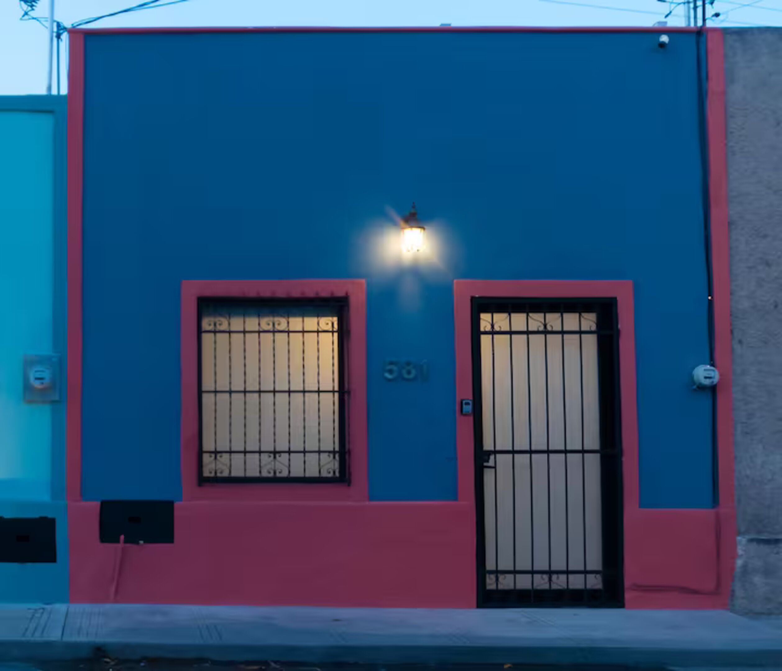 A building with a blue facade, two windows with metal bars, and a door with a metal gate.