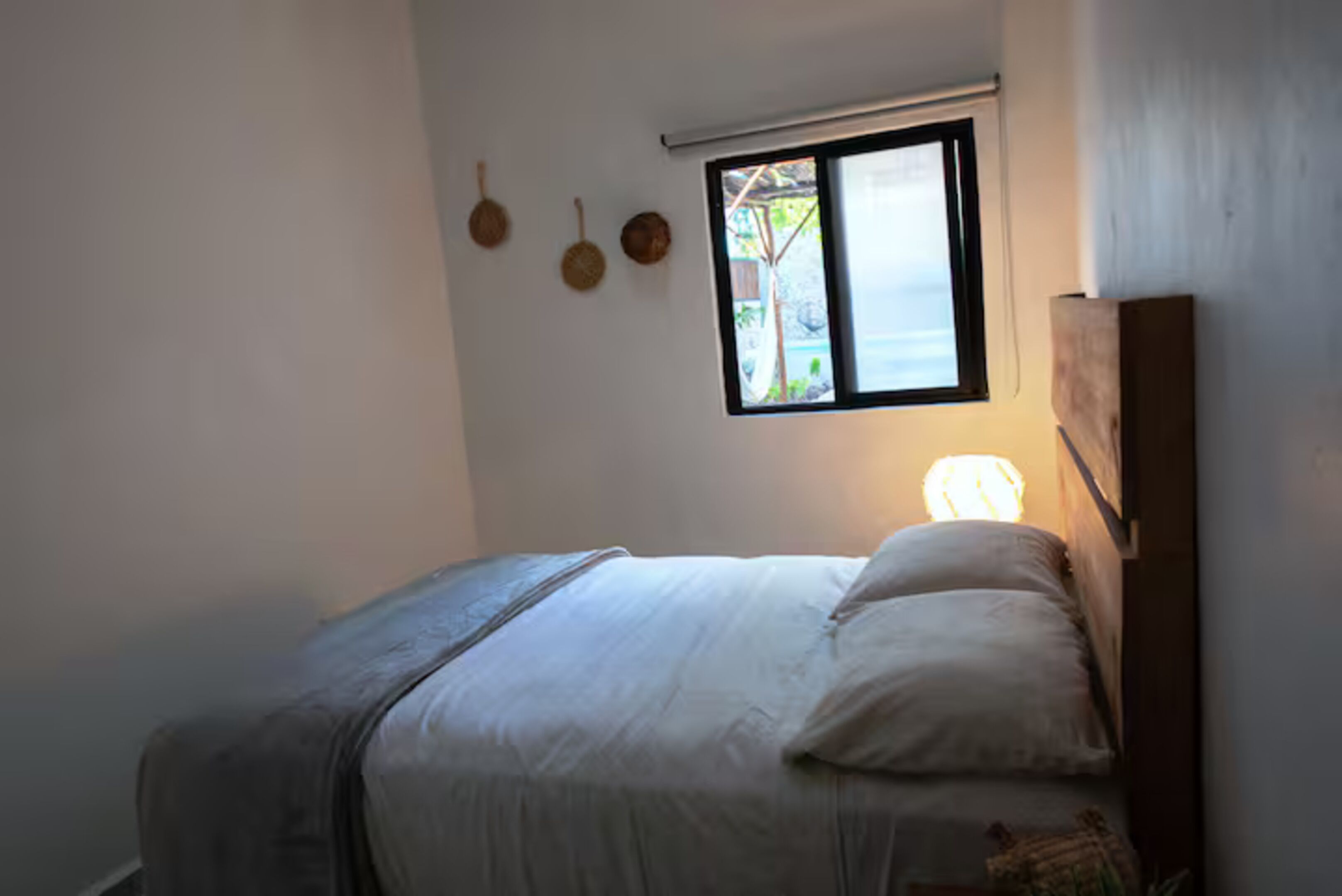 A bedroom with a bed, a window, and a wall-mounted light fixture.