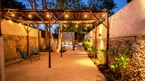 An outdoor patio area with a pergola, string lights, and a pool in the background.
