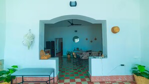 A room with a checkered floor, a ceiling fan, a desk, chairs, a mirror, and a wall-mounted light fixture.