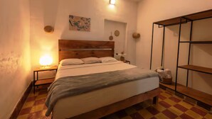 A bedroom with a wooden bed, a nightstand with a lamp, a wall-mounted shelf, and a checkered floor.